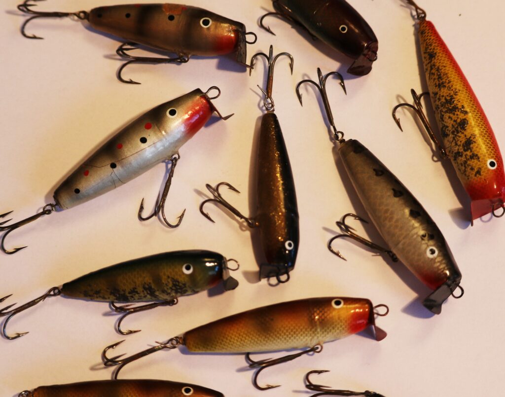 An assortment of colorful fishing lures with treble hooks lies on a light background. The lures vary in patterns and colors, evoking a sense of readiness for fishing.