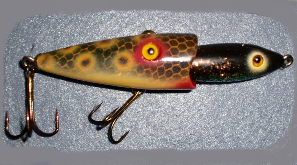 Close-up of a colorful fishing lure with a segmented body, textured scales, and treble hooks on a gray backdrop, evoking an antique feel.
