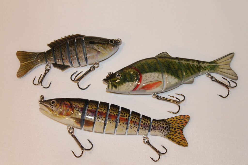 Three colorful, segmented fish lures with realistic patterns and treble hooks on a white background, conveying a sense of dynamic movement.