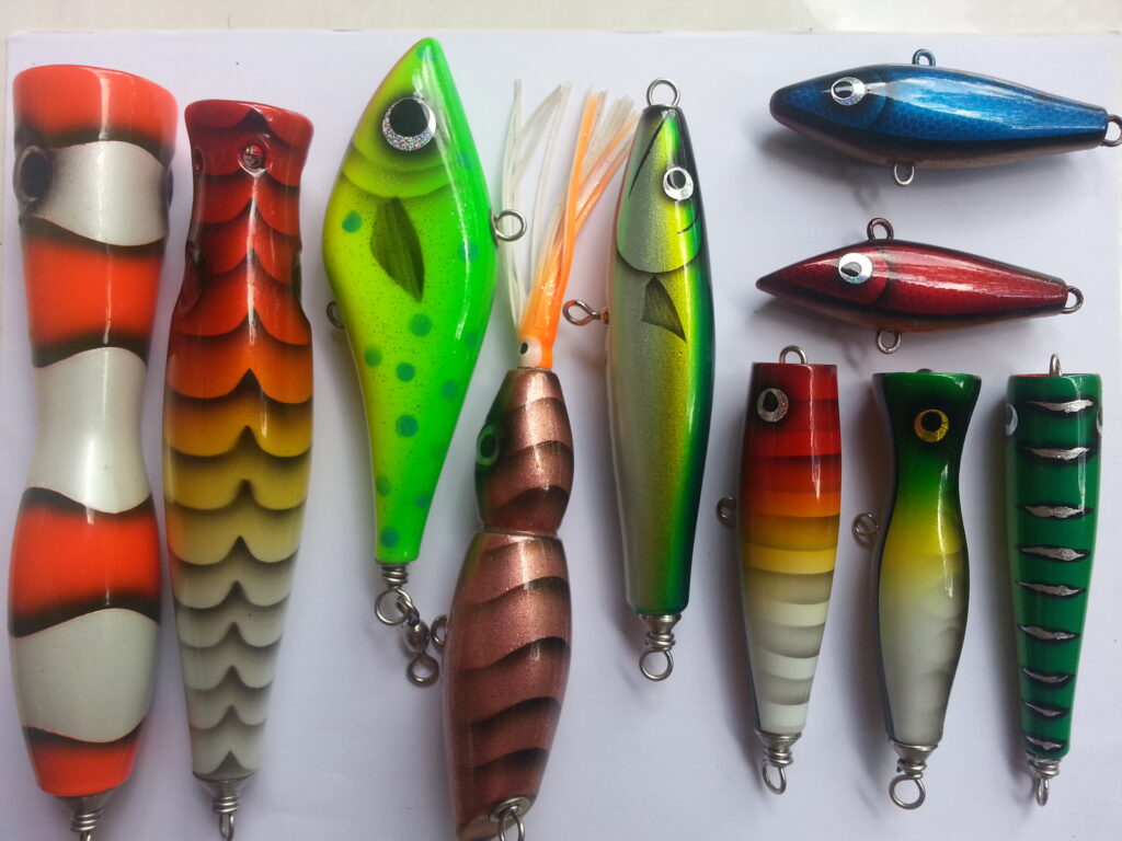 A collection of colorful fishing lures arranged on a white surface. The lures vary in shapes and vibrant colors, including green, red, and blue. Some have eye patterns, stripes, or spots, creating an energetic, alluring display.
