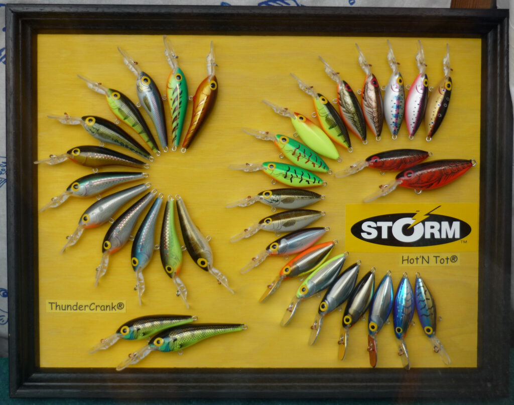 Framed display of colorful fishing lures arranged in a spiral on a yellow background. Includes “ThunderCrank” and “Hot'N Tot” logos, evoking nostalgia.
