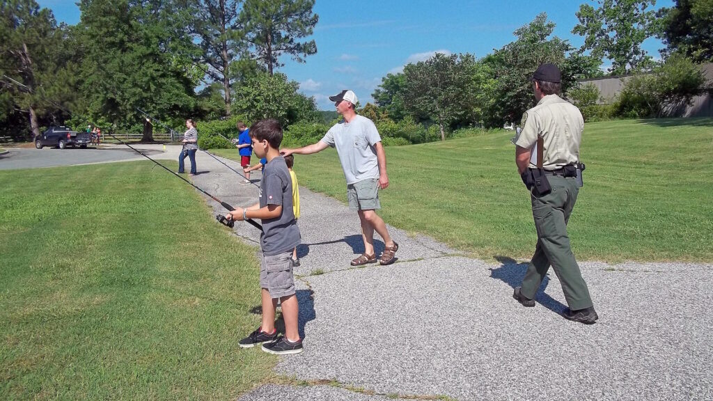A group of children and adults practicing casting with fishing rods on a sunny day,