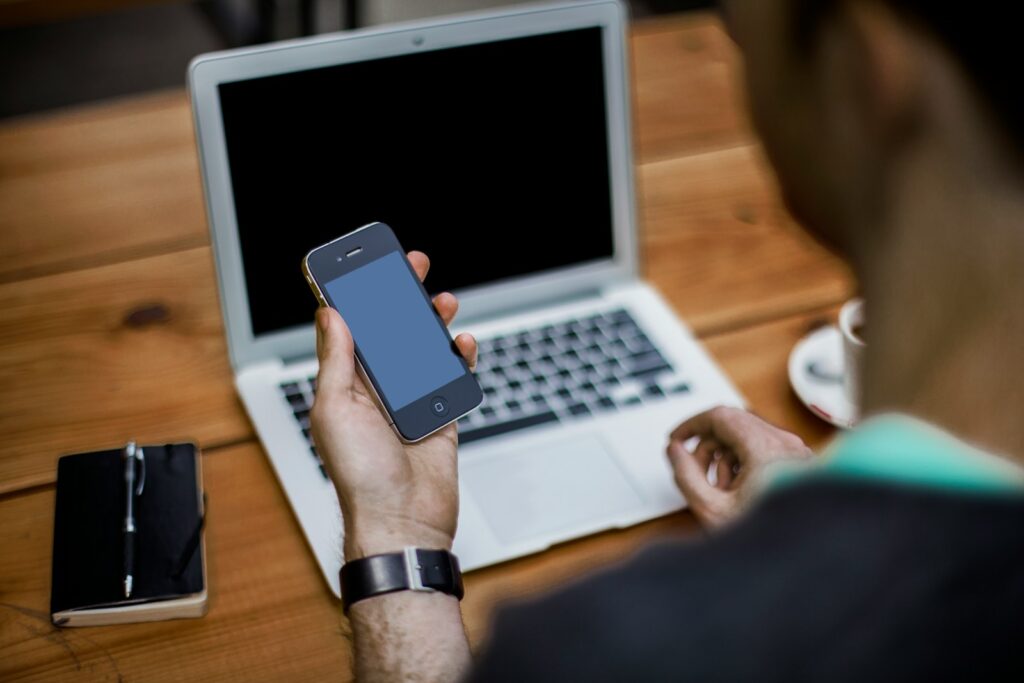 Person holding a black iPhone 4 in front of a MacBook Air.