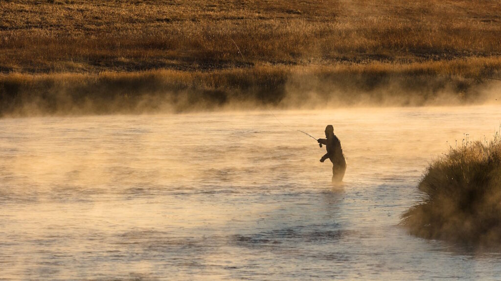 An angler fly fishing in a misty river during early morning in autumn.