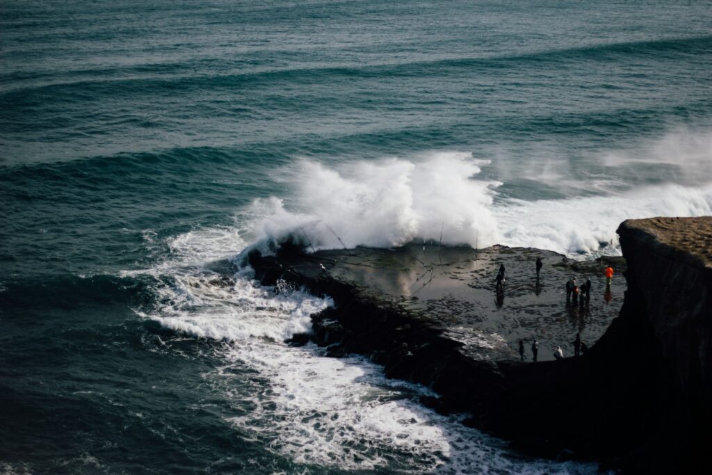 A group of people standing on top of a cliff next to the ocean.