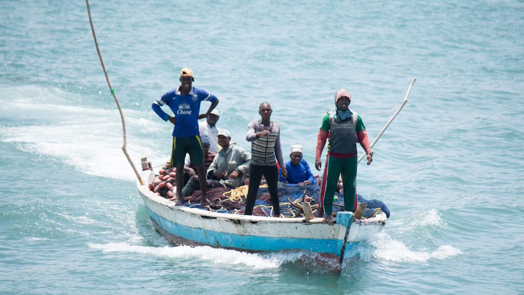 A group of fishermen in a wooden boat on a calm river, actively engaged in fishing
