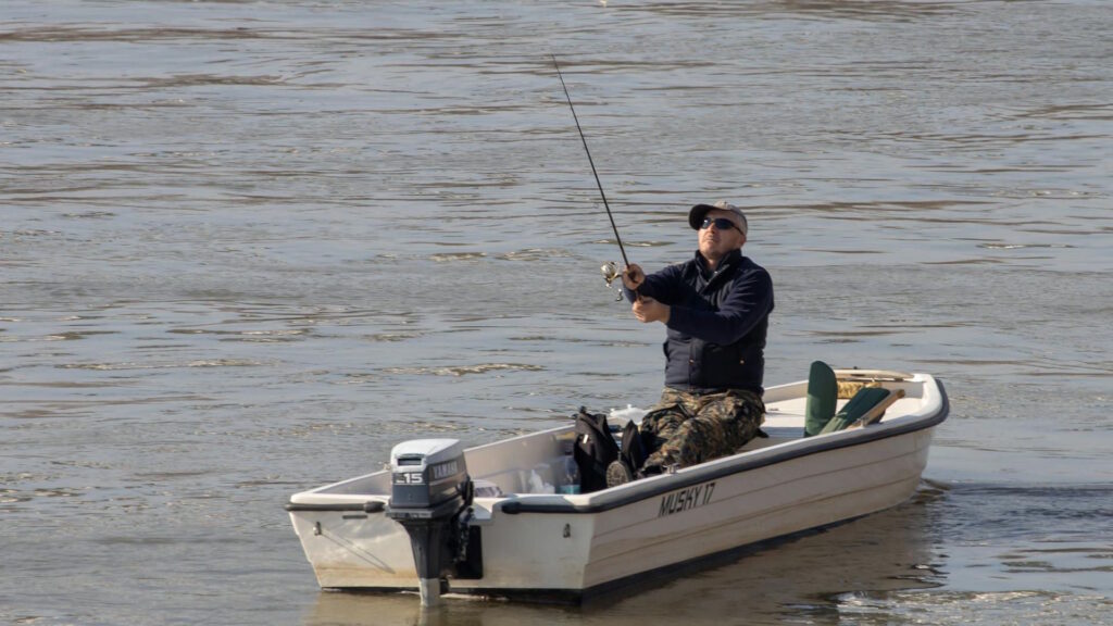 Fisherman on a motorboat casting a fishing line into clear water