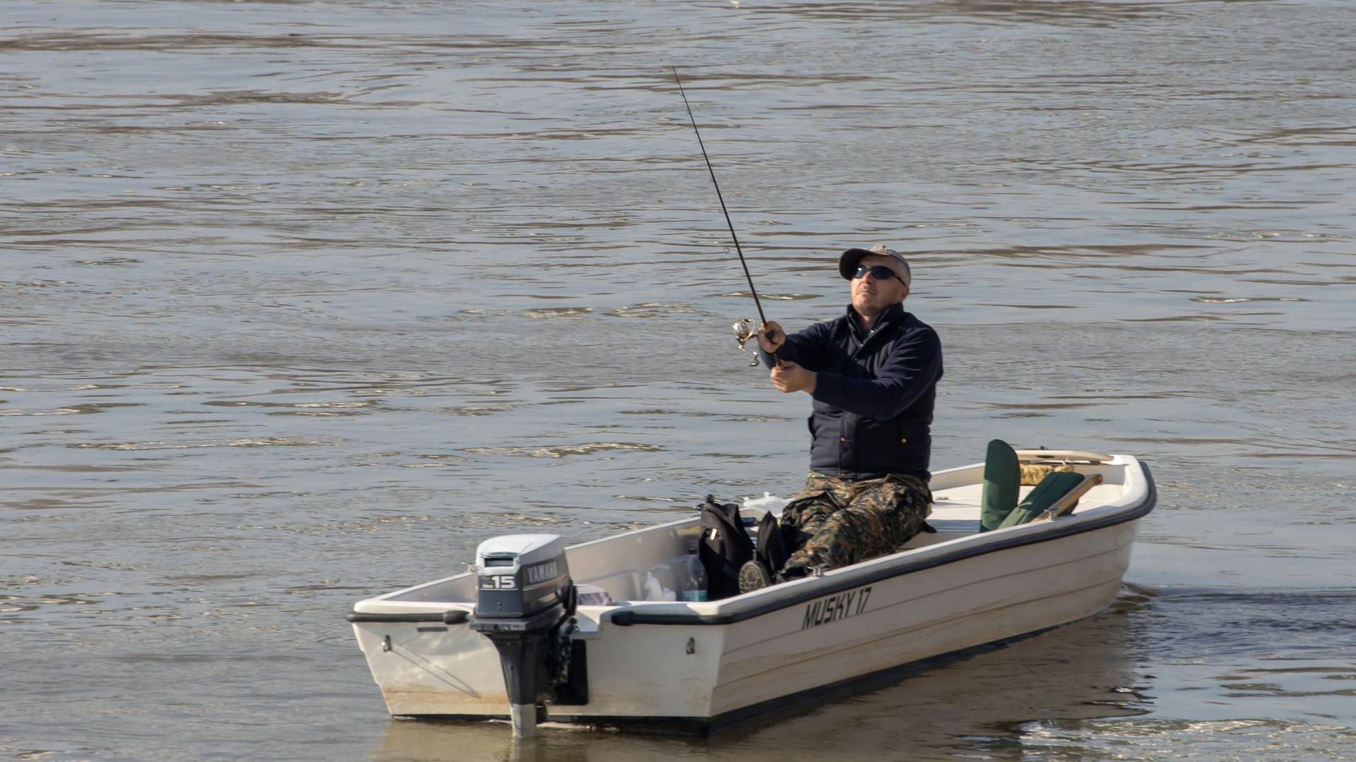 Fisherman on a motorboat casting a fishing line into clear water