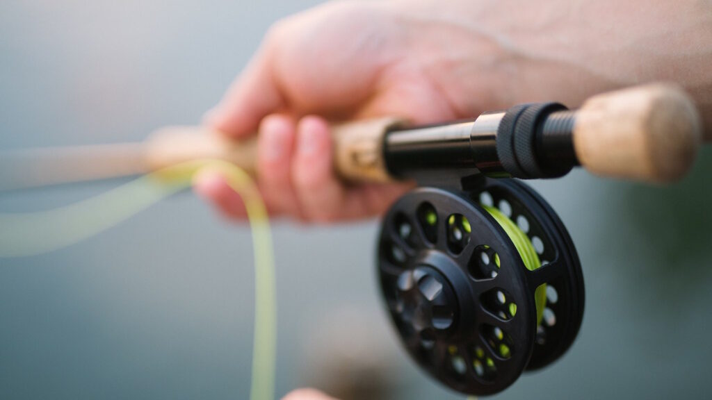 A close-up of a person's hand holding a fishing rod with a reel and bright yellow fishing line.