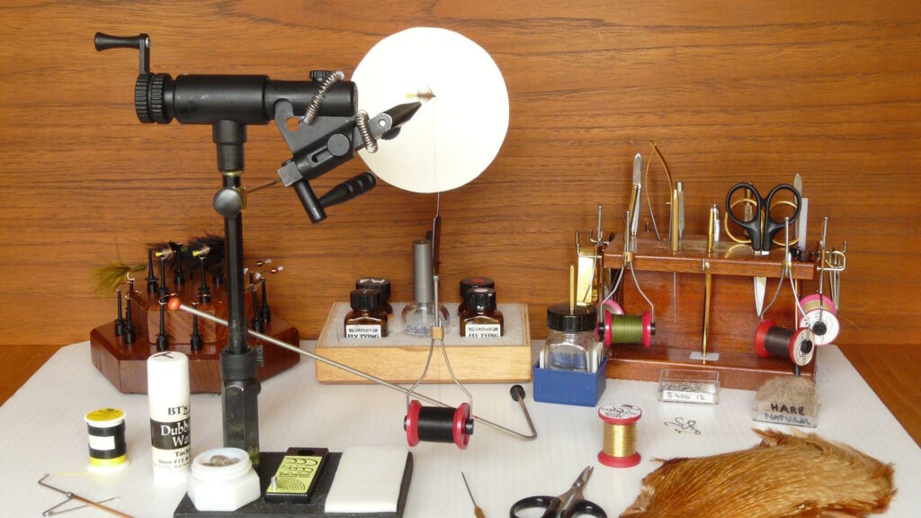 Fly dressers workbench, showing various tools various tools, feathers, threads, and materials organized for fly creation.