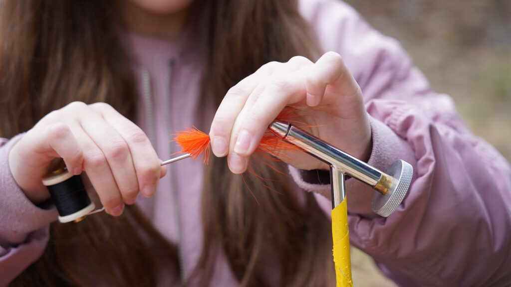 Student wrapping thread around her bright orange fishing fly
