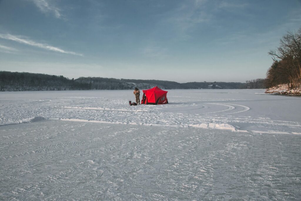 A person is outside the tent in a snow-covered field during the day.
