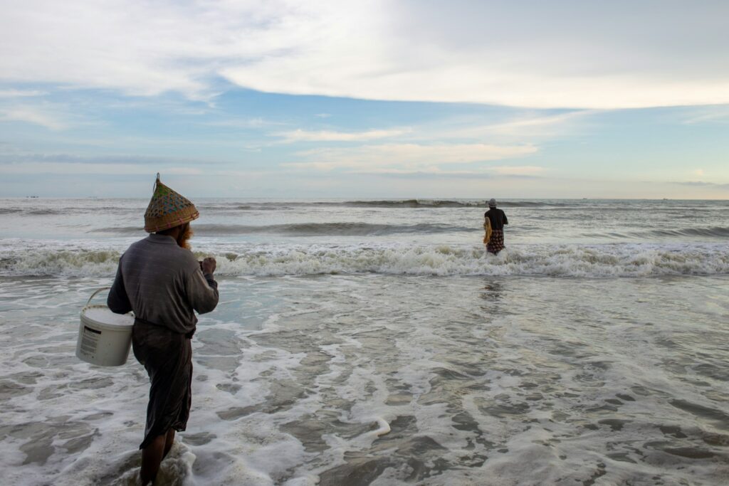 A man standing in the ocean holding a bucket.