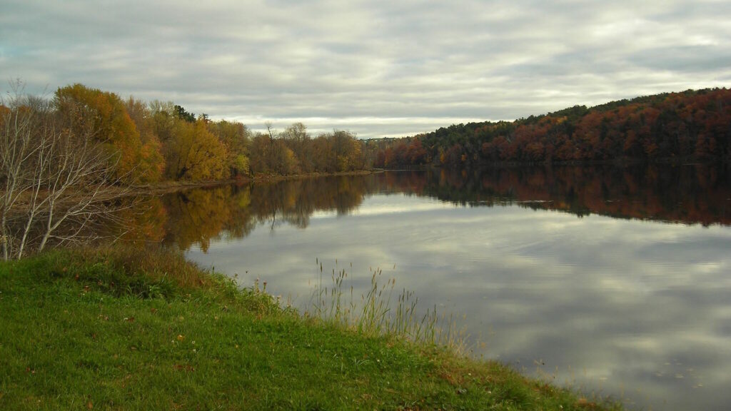 Calm river surrounded by colorful autumn trees under a cloudy sky.