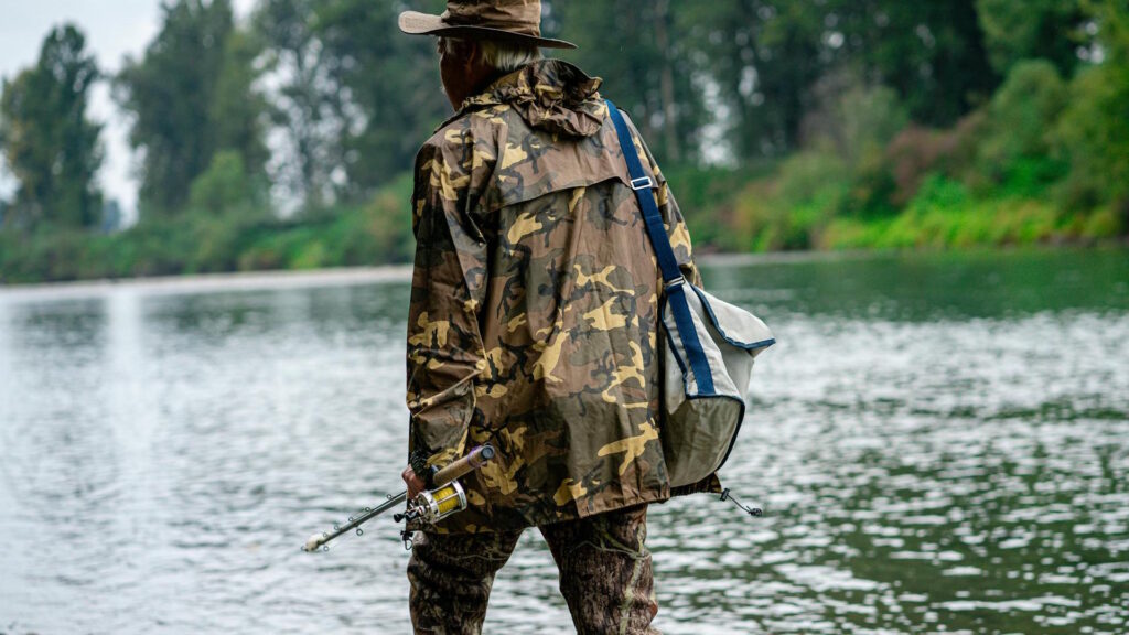 Man in Camouflage Top and Pants Walking on Shore with Fishing Rod