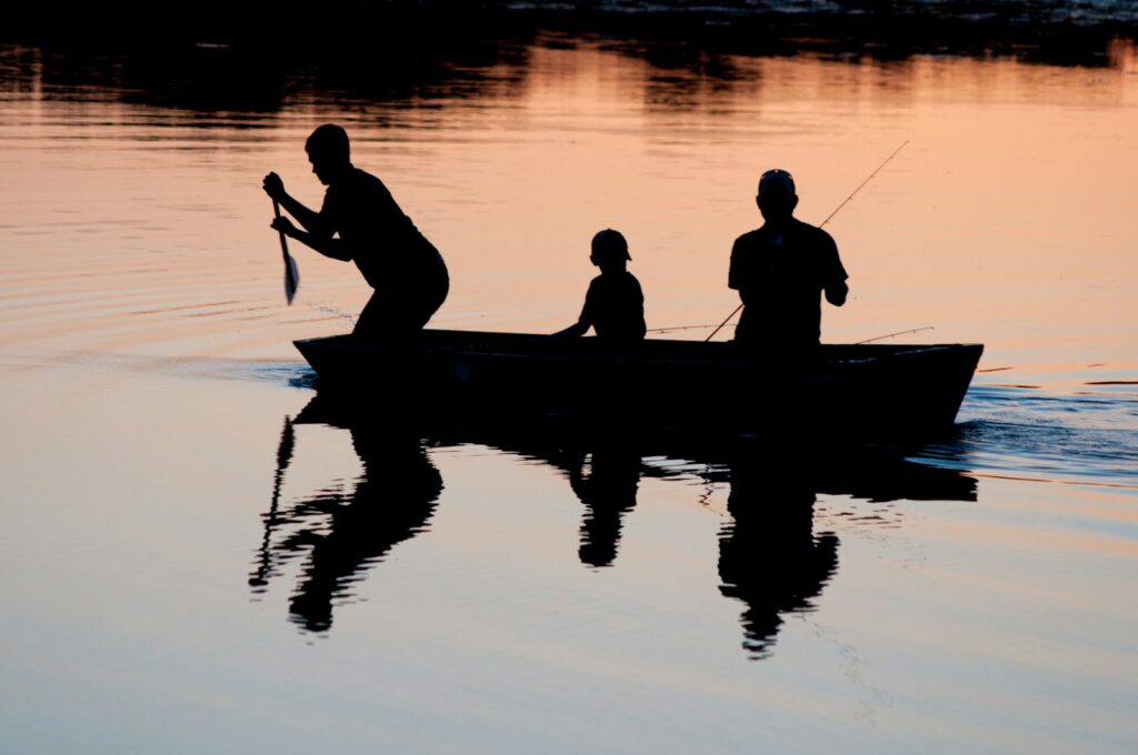 Silhouette of three person riding on boat on body of water.