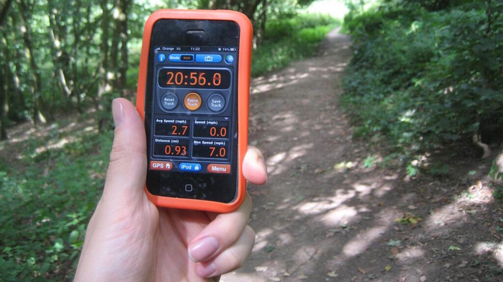 Person using a GPS tracking app on a smartphone while walking through a forest path.