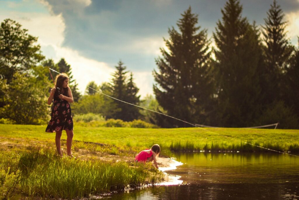 A girl is fishing beside a lake during the day.