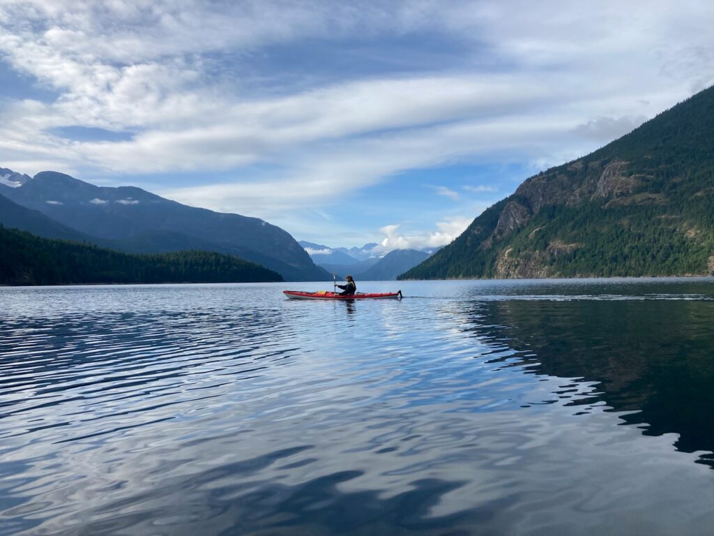 A person in a canoe on a lake with mountains in the background.