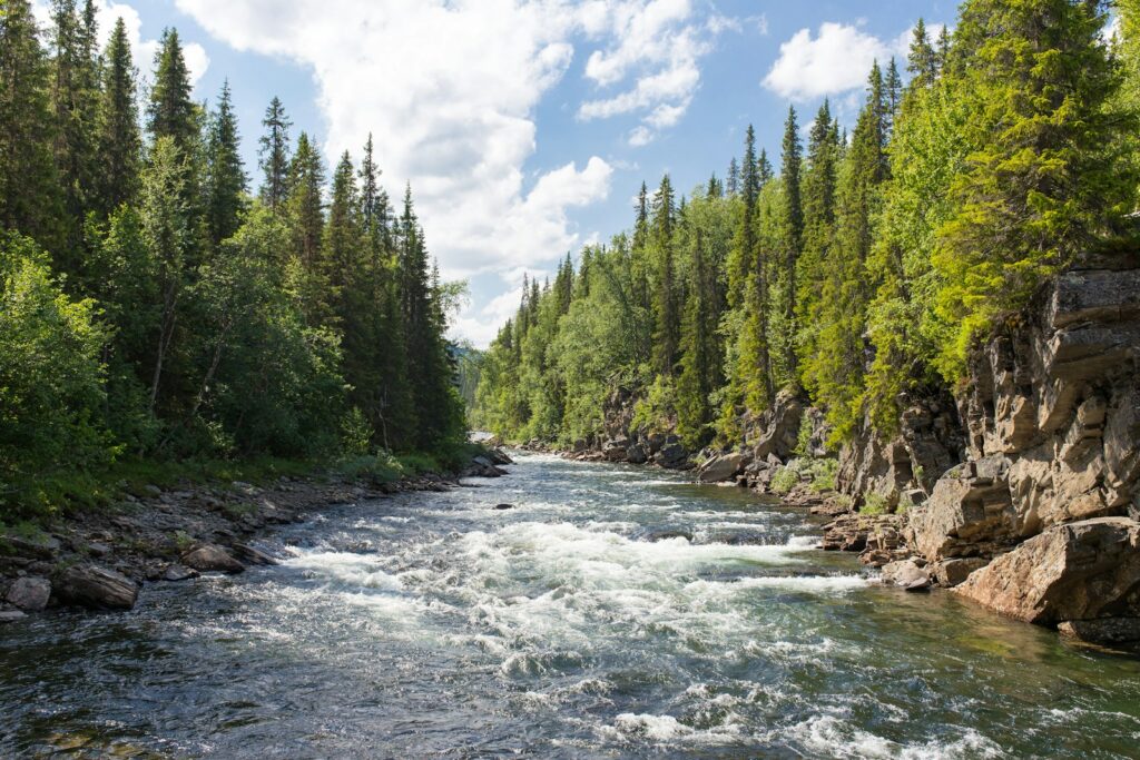River between grassy cliffs under cloudy sky.