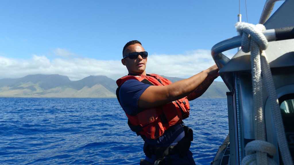 U.S. Coast Guard officer on a patrol boat wearing a life vest and sunglasses.