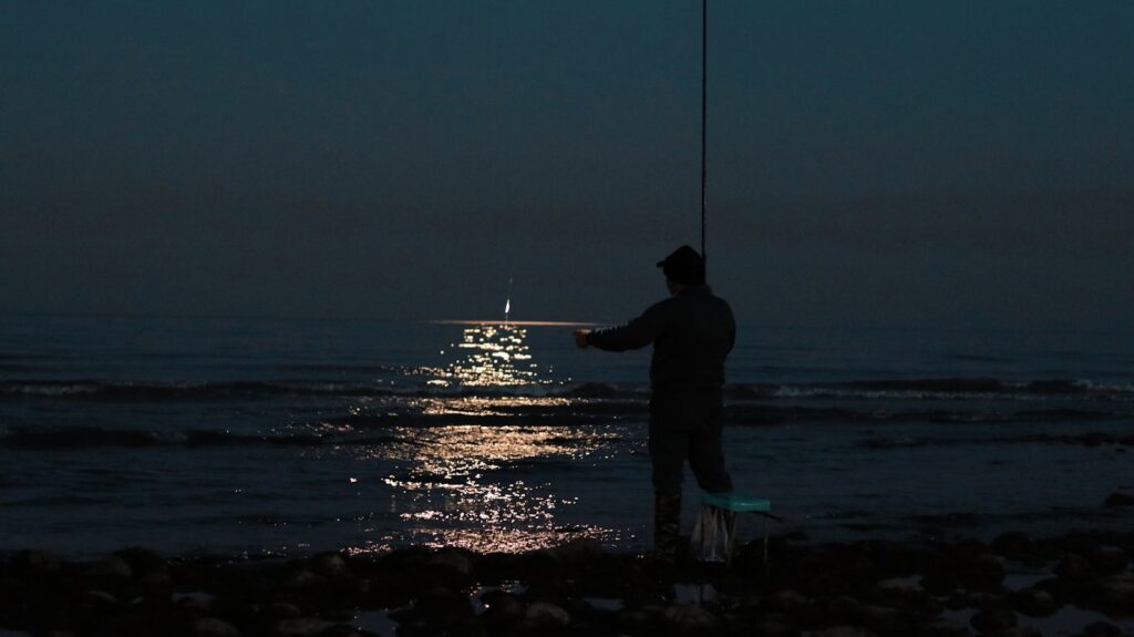 A man fishing on the ocean at night.