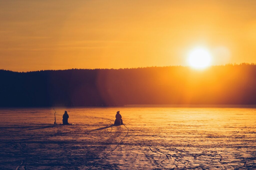 Silhouette of 2 people ice fishing during sunset.