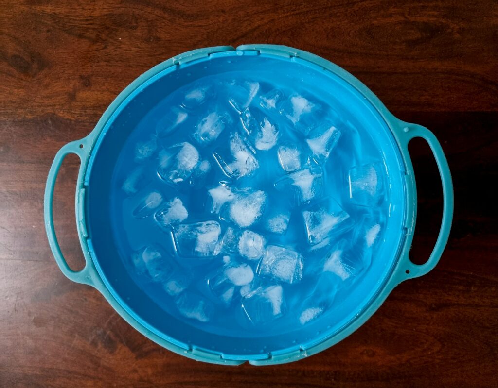 An ice bucket filled with ice cubes on top of a wooden table.