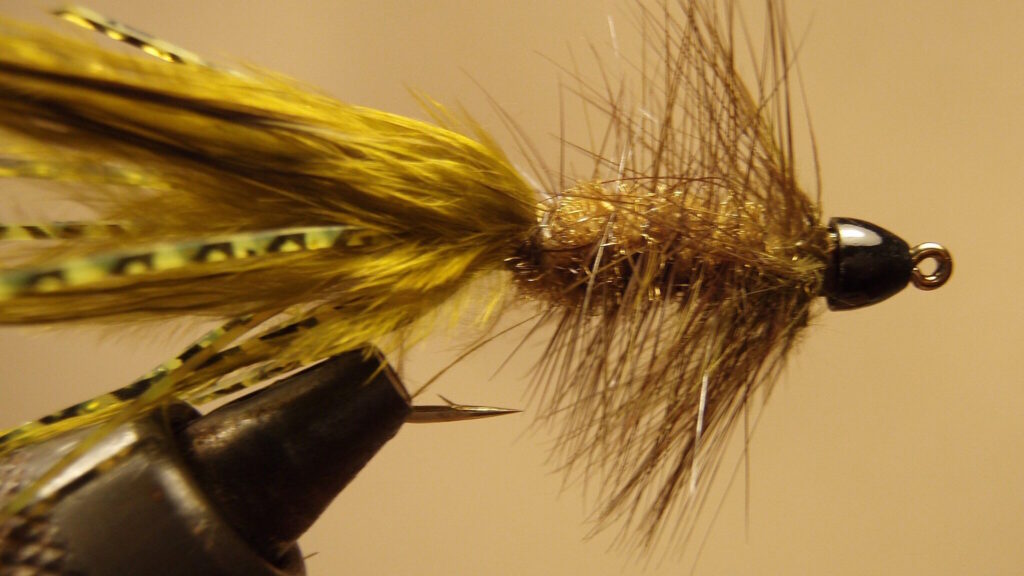 Close-up of a finished Woolly Bugger fly with olive marabou tail, chenille body, and hackle wrapped around the shank.