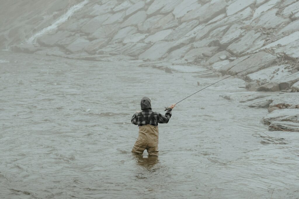 A man standing in a river while holding a fishing pole.
