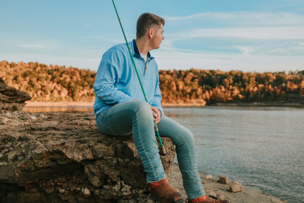 A man sitting on top of a rock next to a body of water.