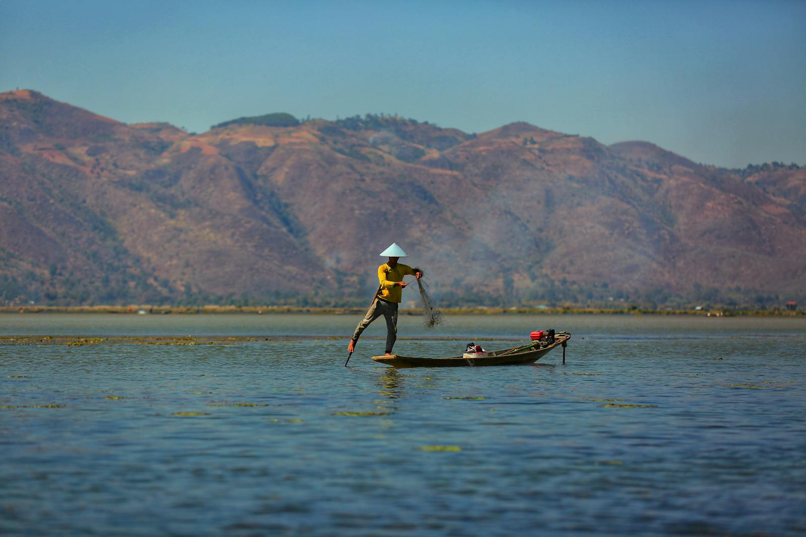 Fisherman casting net on Inle Lake in Shan State, Myanmar, showcasing traditional fishing.