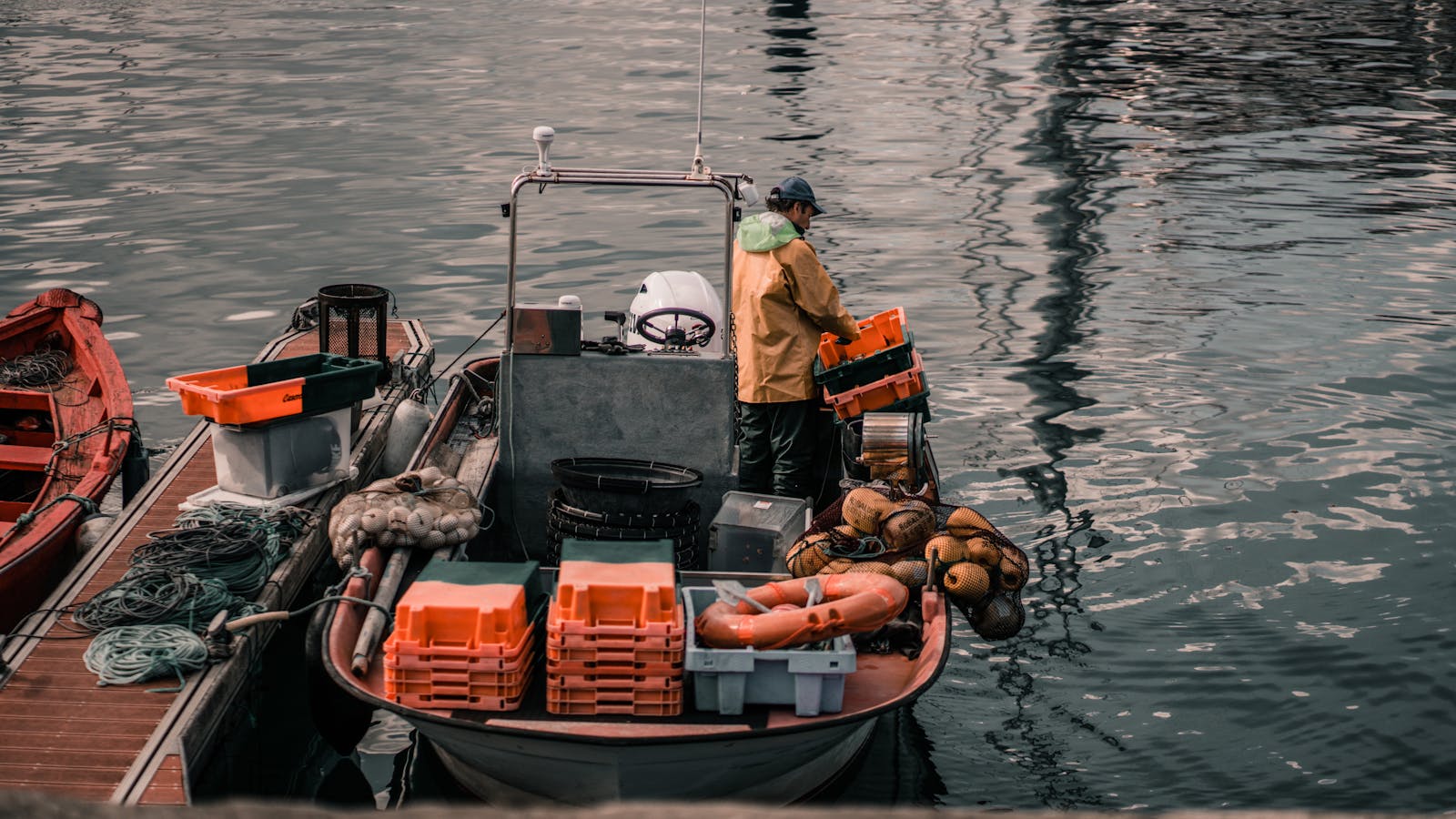 A fisherman in a yellow coat works on a motorboat, organizing fishing gear at a harbor in La Coruña, Spain.