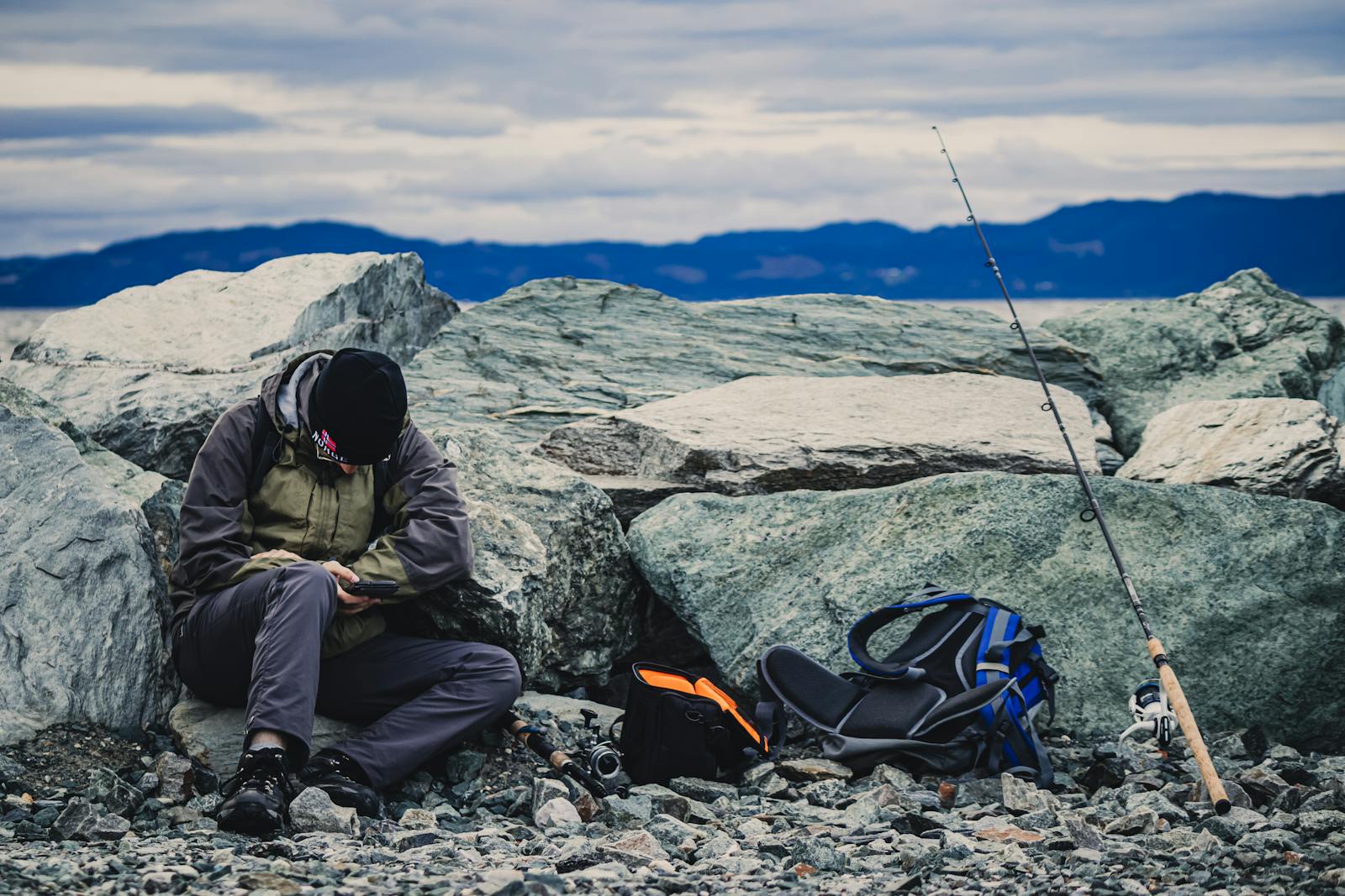 Man relaxing on rocky shore with fishing gear in Trondheim, Norway.