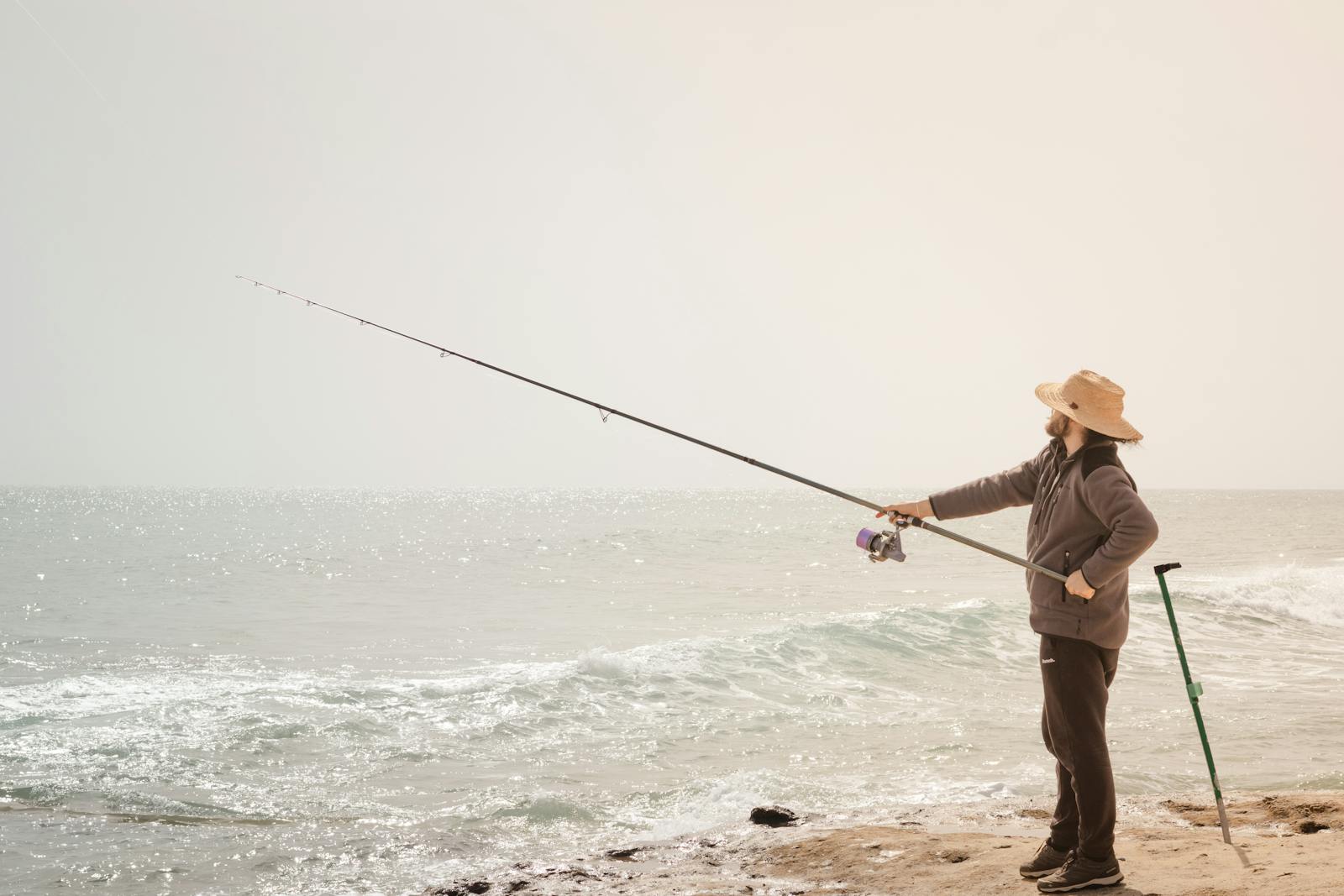 A man fishing with a rod by the sea, enjoying a sunny day on the beach.
