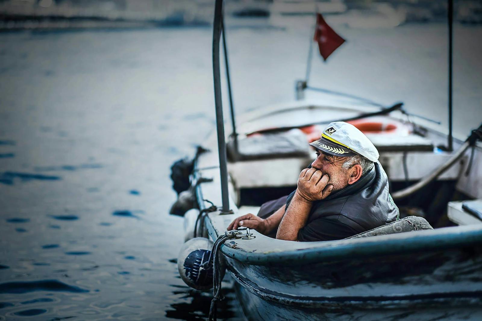 Elderly sailor in a boat gazing thoughtfully at the sea with a distant horizon background.