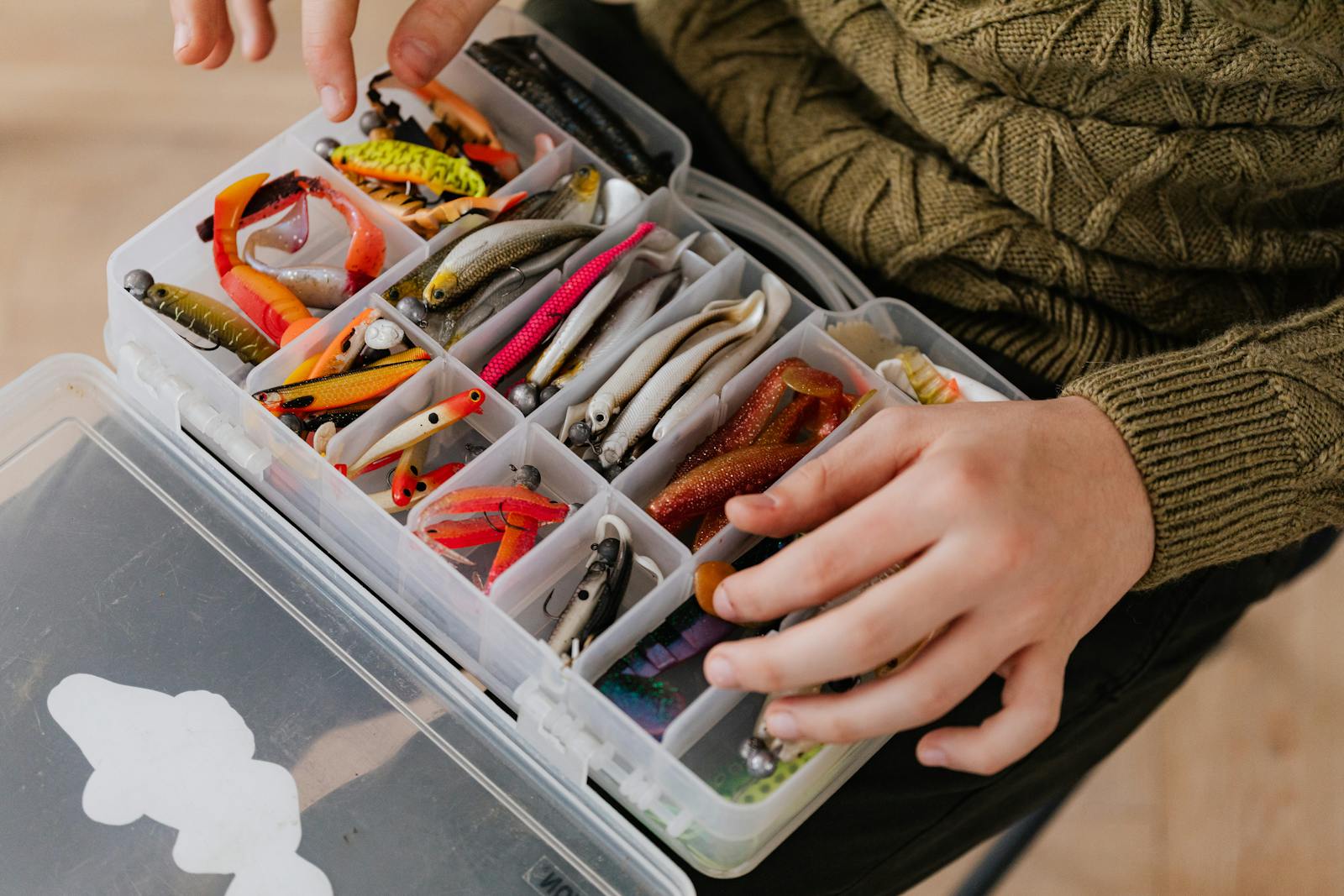 Close-up of assorted fishing lures neatly arranged in a plastic tackle box held by a person.