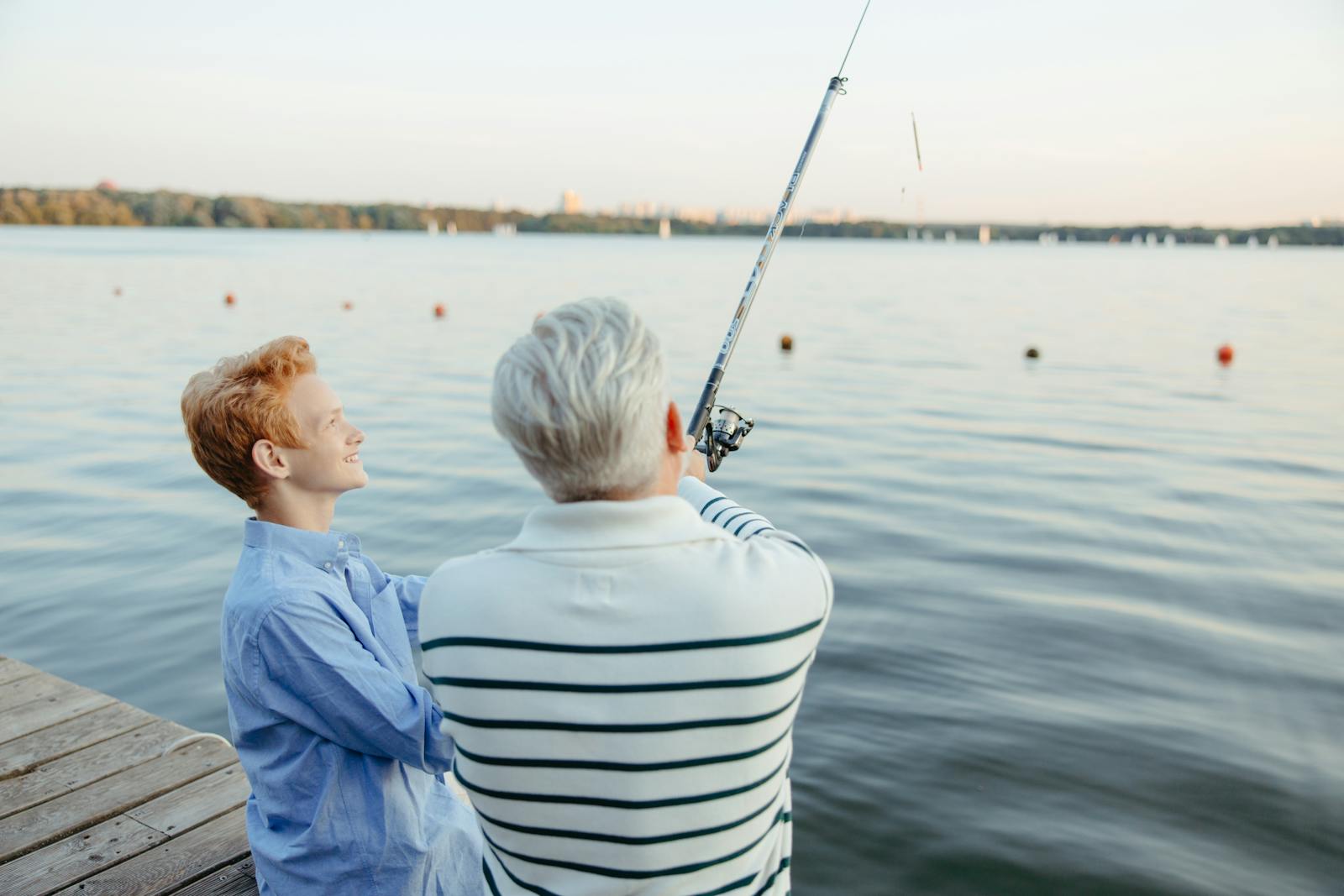 A grandfather and grandson enjoying a peaceful fishing trip on a dock by the ocean.