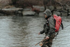 A man with a red backpack and a fishing pole.