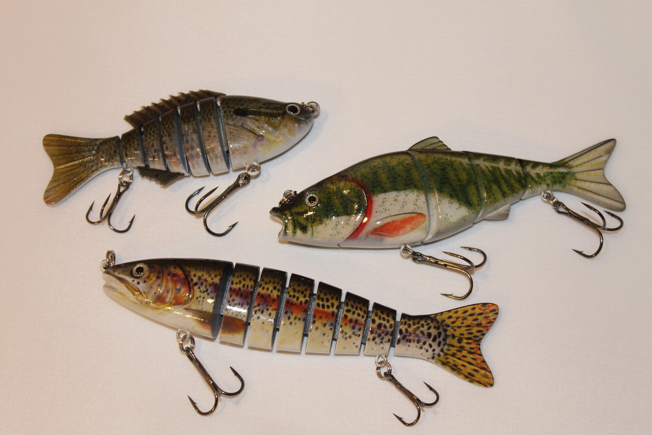 Three colorful, segmented fish lures with realistic patterns and treble hooks on a white background, conveying a sense of dynamic movement.