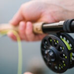 A close-up of a person's hand holding a fishing rod with a reel and bright yellow fishing line.