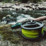 A reel and a spool of water sitting on a rock next to a river.