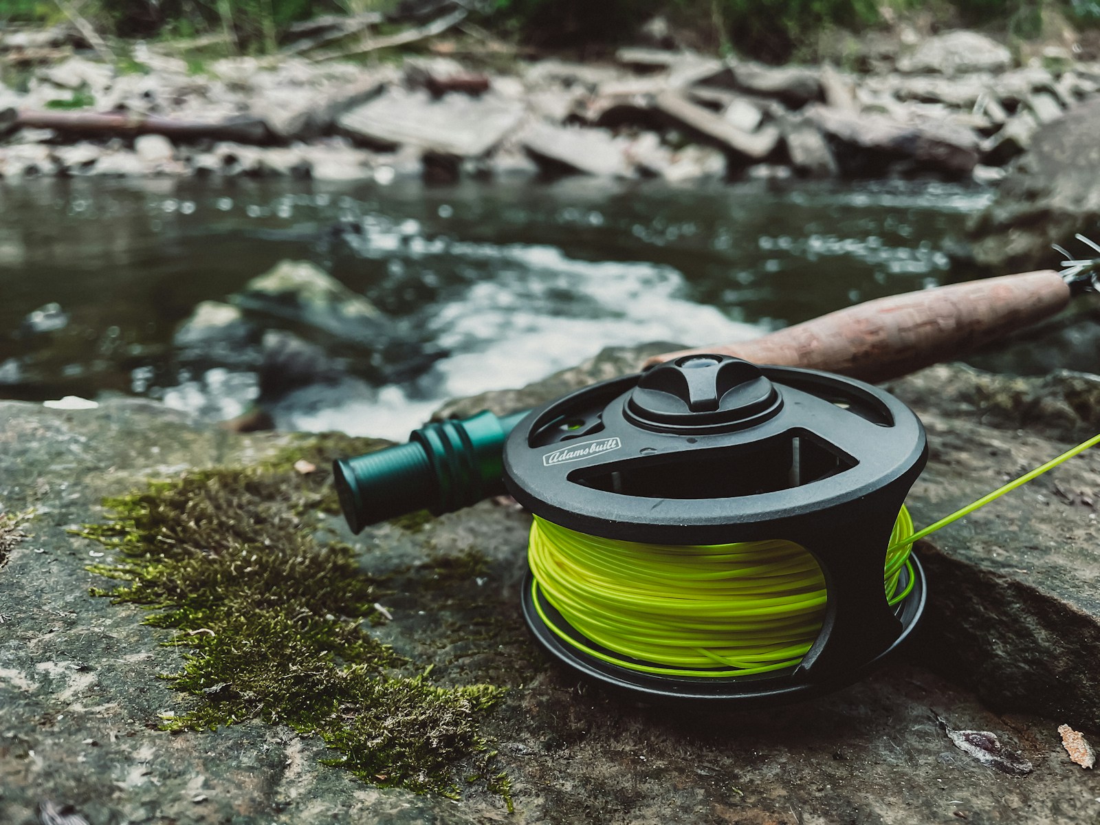 A reel and a spool of water sitting on a rock next to a river.